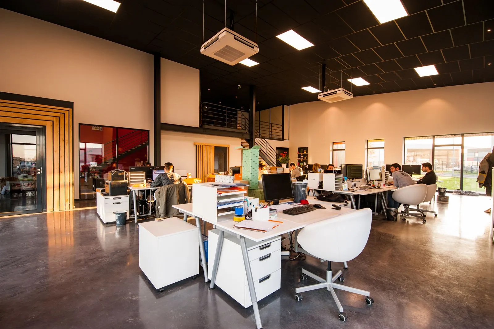 Interior de oficinas con mesas de madera, sillas negras y luz natural.